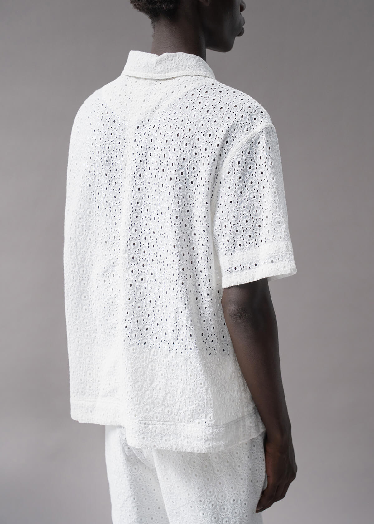 Person wearing a white embroidered shirt and pants on a gray background